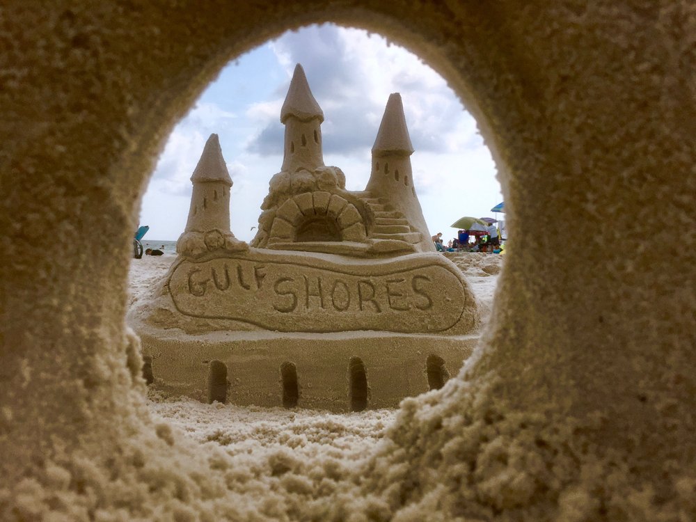 Looking through a carved archway of a sandcastle toward the ocean beyond