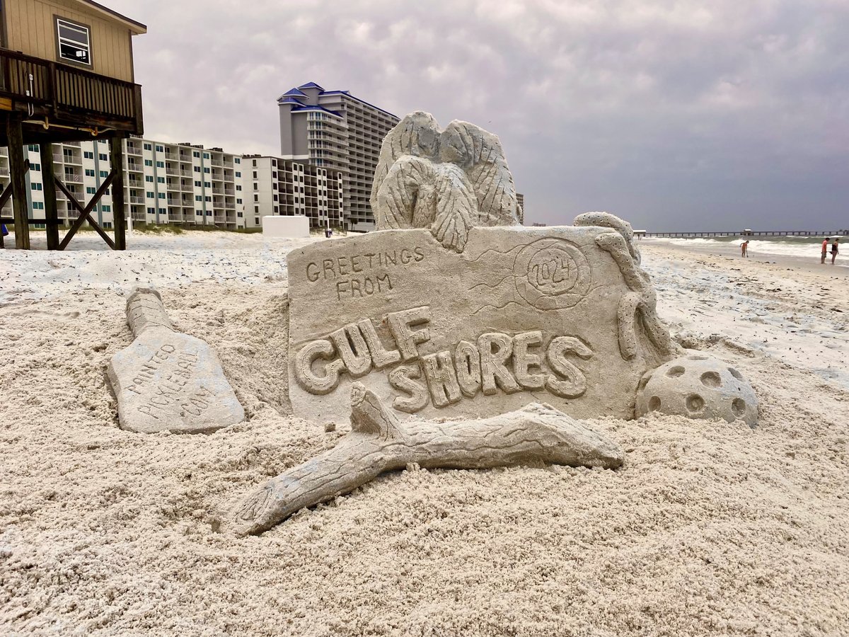 A sand sculpture reading Greetings From Gulf Shores with a sculpted pickleball and paddle
